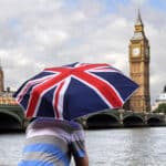 ourist holding a UK flag umbrella near Big Ben in London – UK visa from Dubai travel concept